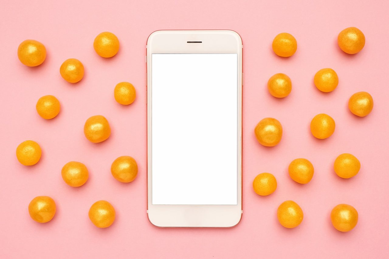 mobile-phone-and-sweet-yellow-candies-on-a-pink-background-technology-mock-up.jpg